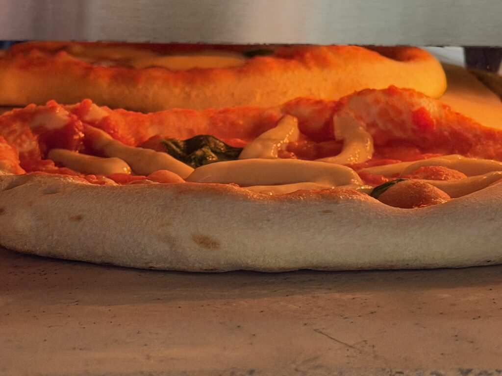 Blick in den Tentazione GT4 Max Pizzaofen – Pizza auf Biscotto-Stein mit sichtbarem Spiegel-Effekt an der Rückwand