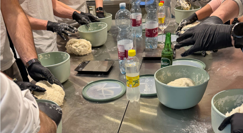 Hände beim Teig kneten – Workshopleiter zeigt Teilnehmer die richtige Technik beim Pizza Kurs