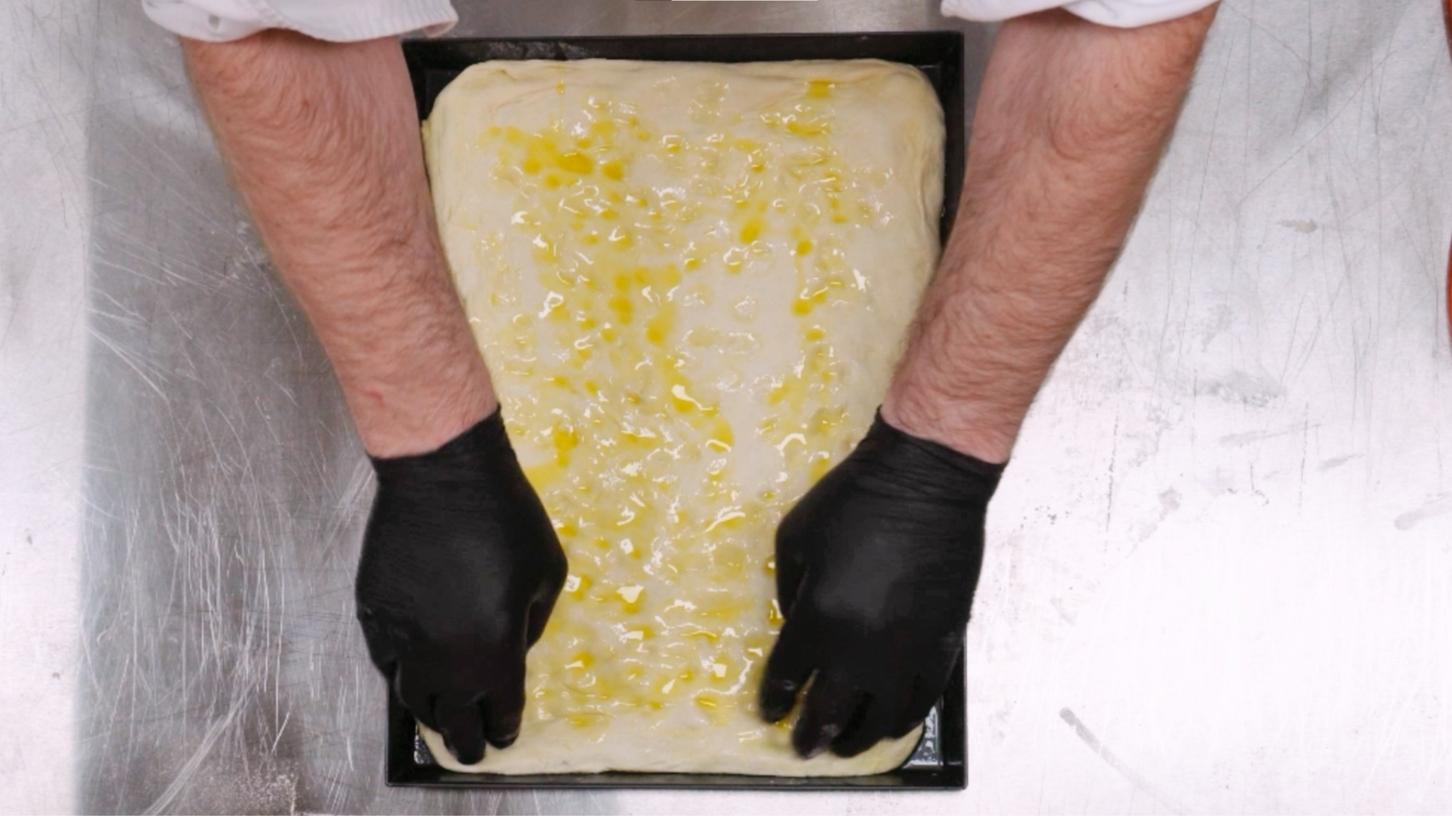 Focaccia-Teig auf dem Backblech mit Olivenöl beträufelt – vor dem Backen