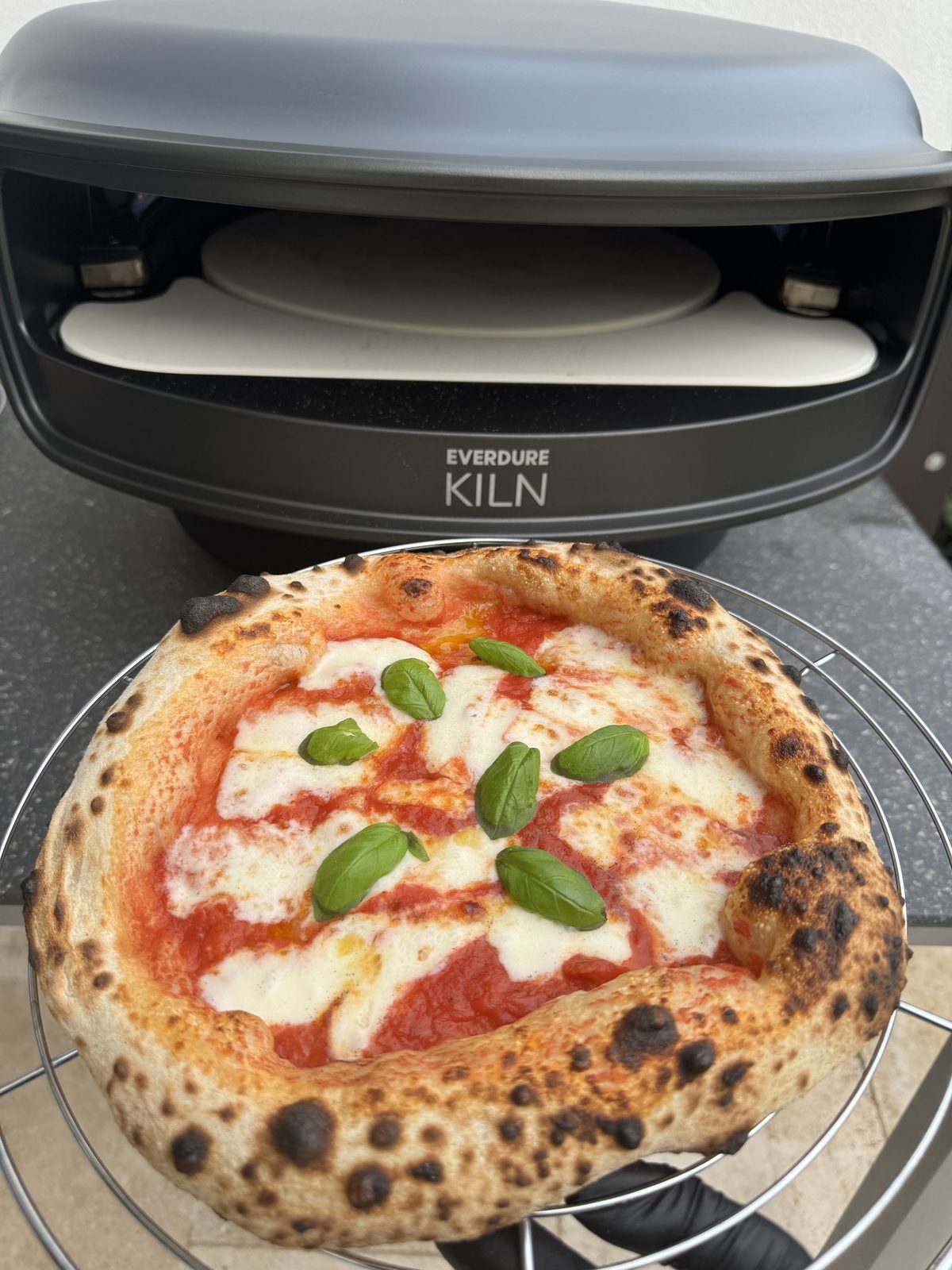 Margherita mit dunklen Leopardenflecken am aufgeblasenen Cornicione neben dem Gas-Pizzaofen