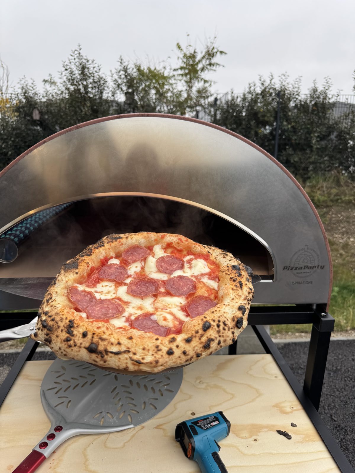 Pizza wird bei hoher Hitze aus dem Gas-Pizzaofen gezogen, Infrarot-Thermometer und Turning Peel daneben