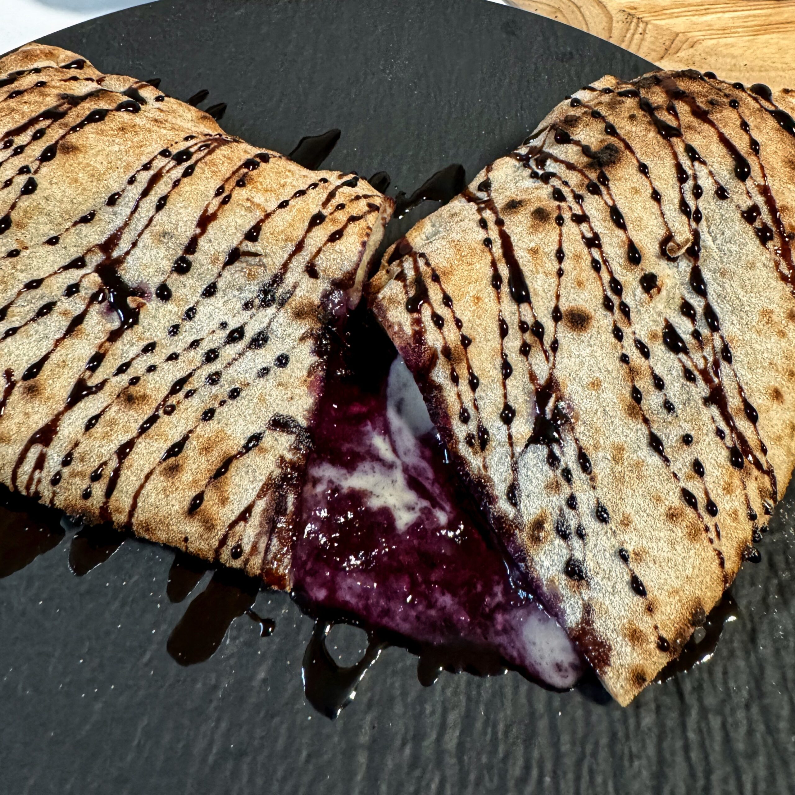 Süße Calzone mit Heidelbeer-Vanillepudding-Füllung, Schokosauce und Puderzucker, aufgeschnitten