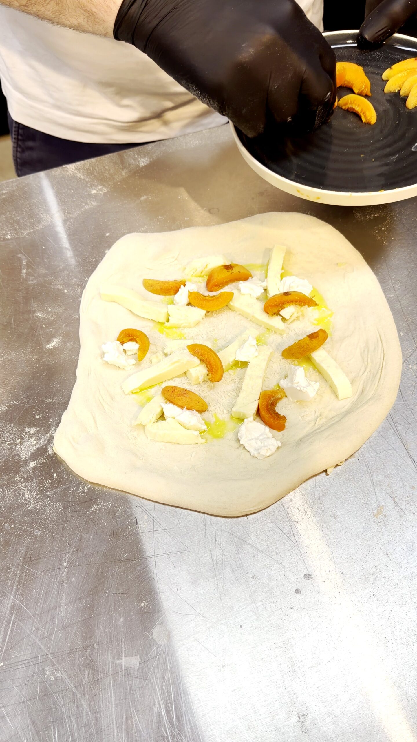 Pizzateig wird mit Fior di Latte, Ricotta und Marillenspalten belegt