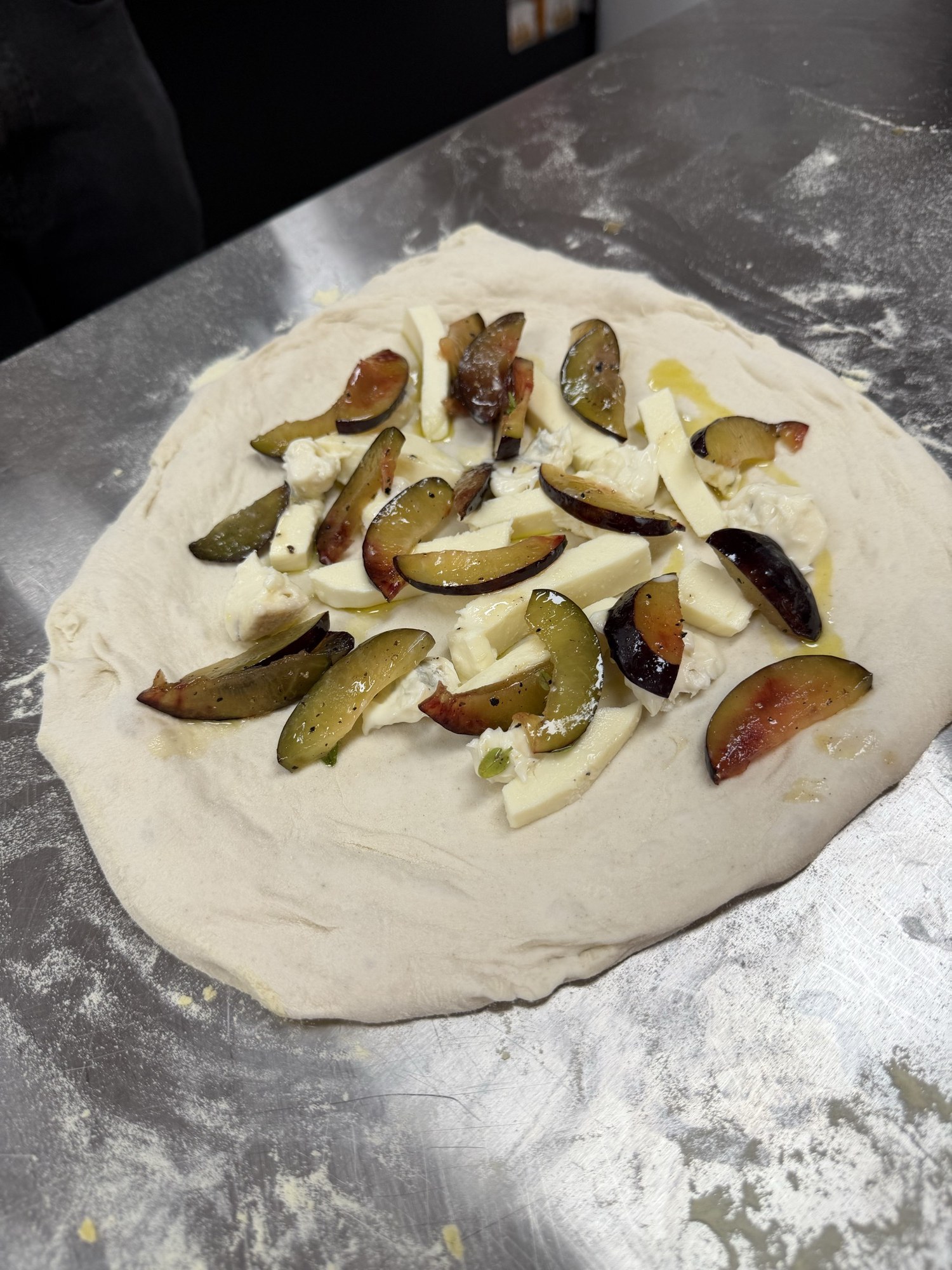 Pizzateig mit Fior di Latte, Gorgonzola und marinierten Zwetschgenspalten belegt, vor dem Backen