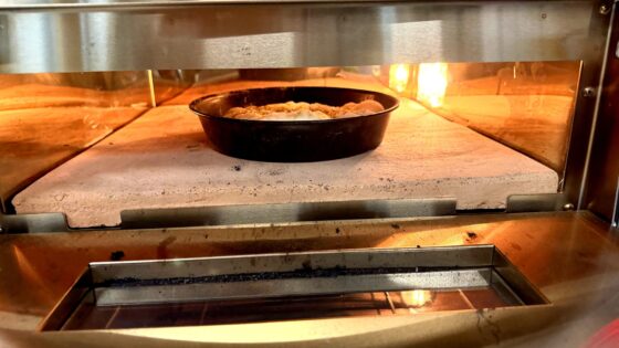 Runde Blaublechform mit Brot aus Pizzateig im Pizzaofen bei geoeffneter Tuer