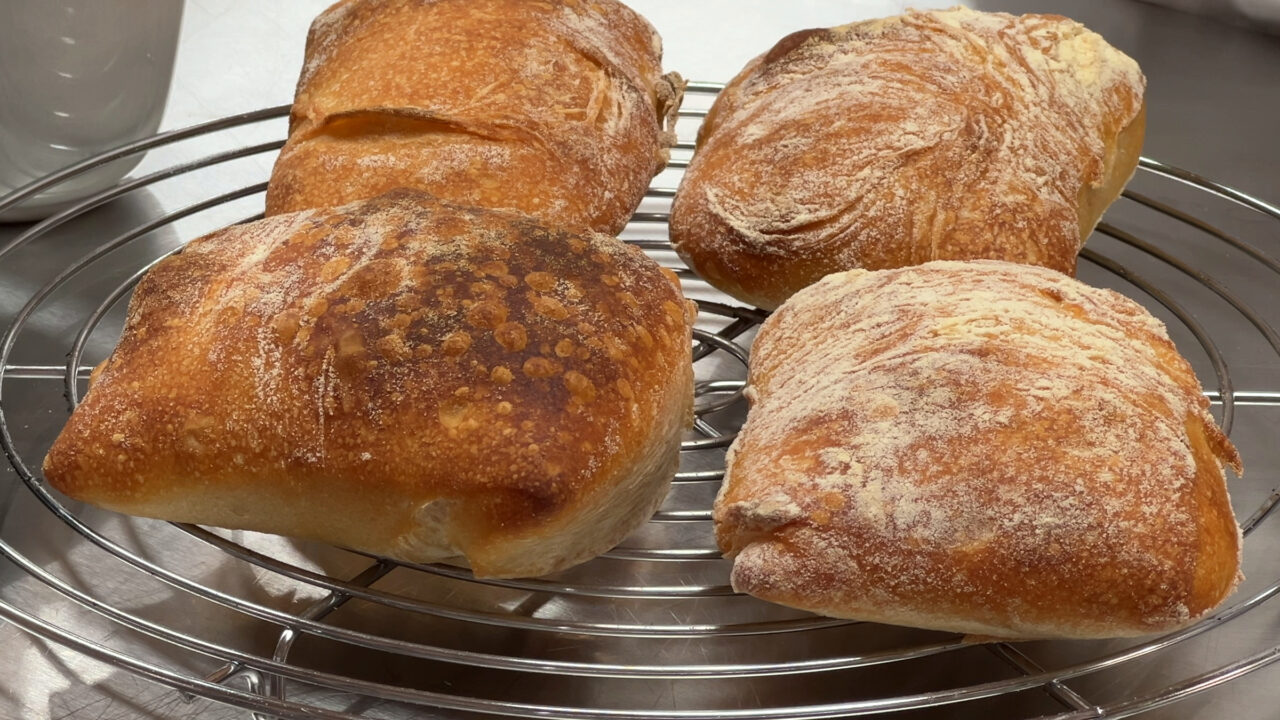 Vier goldbraune Mini-Ciabatta aus Pizzateig auf einem Auskühlgitter