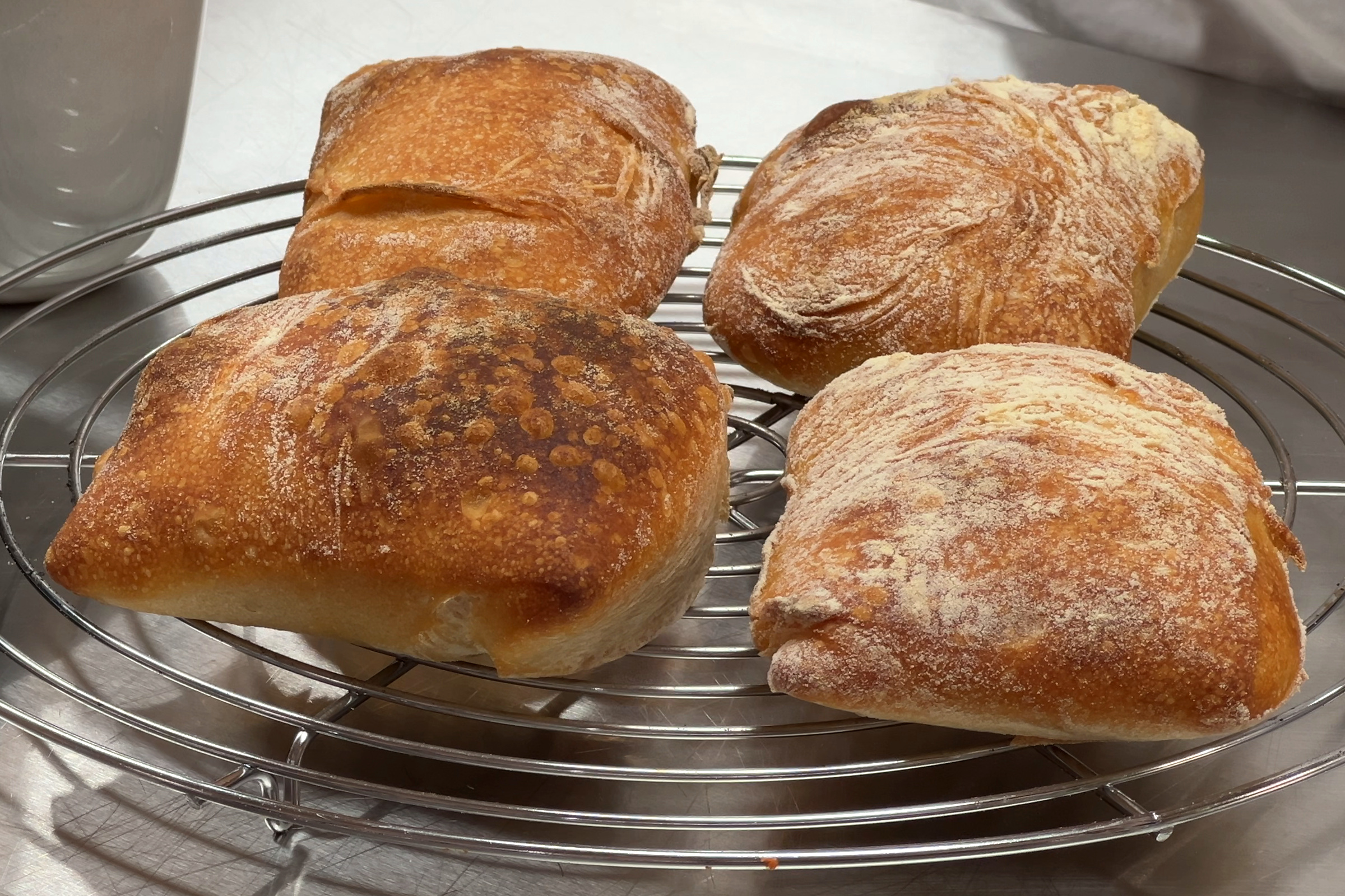 Vier goldbraune Mini-Ciabatta aus Pizzateig-Resten auf einem Auskühlgitter