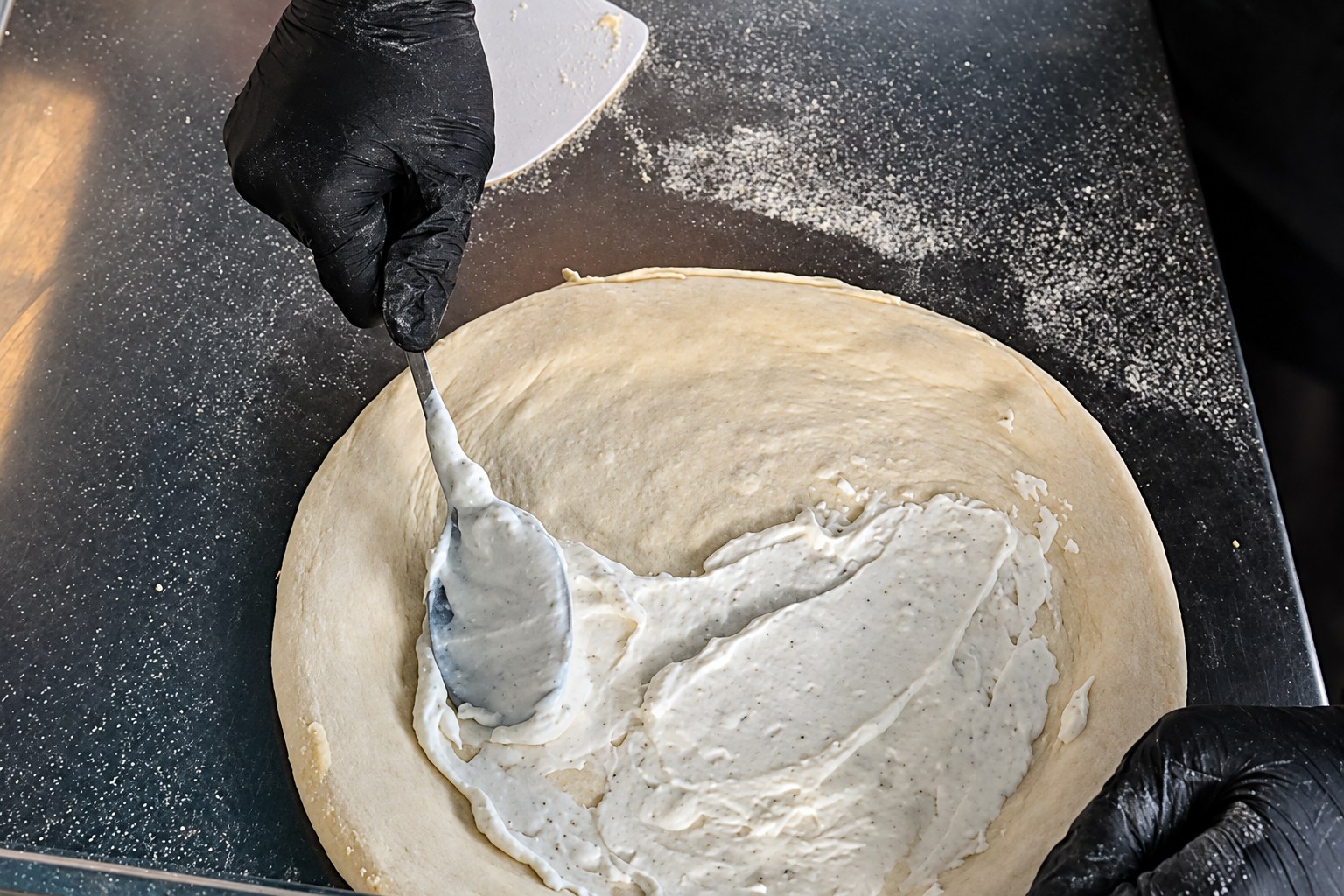 Weiße Ricotta-Sauce wird mit dem Löffel als Base auf den ausgezogenen Pizzateig gestrichen
