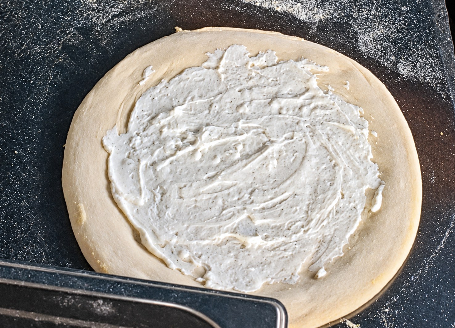 Pizzateig mit gleichmäßig verteilter weißer Ricotta-Sauce, Rand frei gelassen