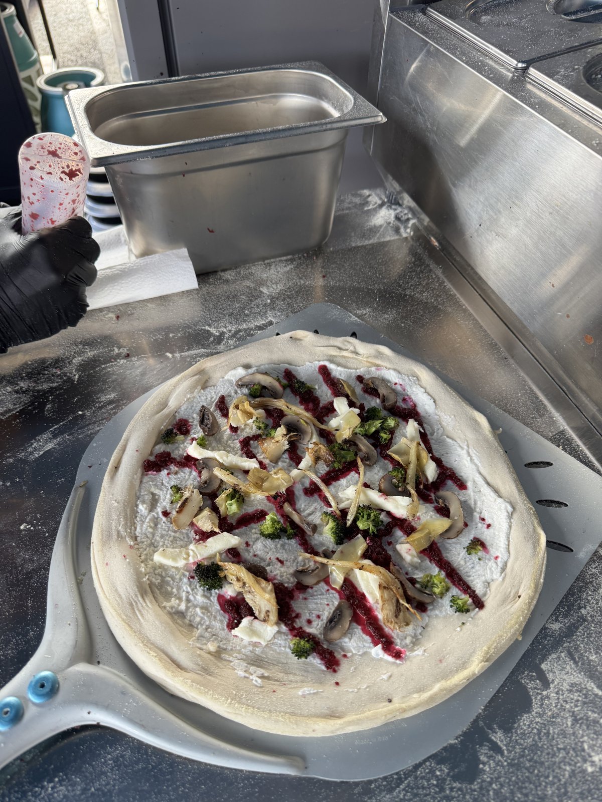 Belegte vegetarische Pizza mit Brokkoli, Fenchel und Champignons auf der Pizzaschaufel vor dem Backen